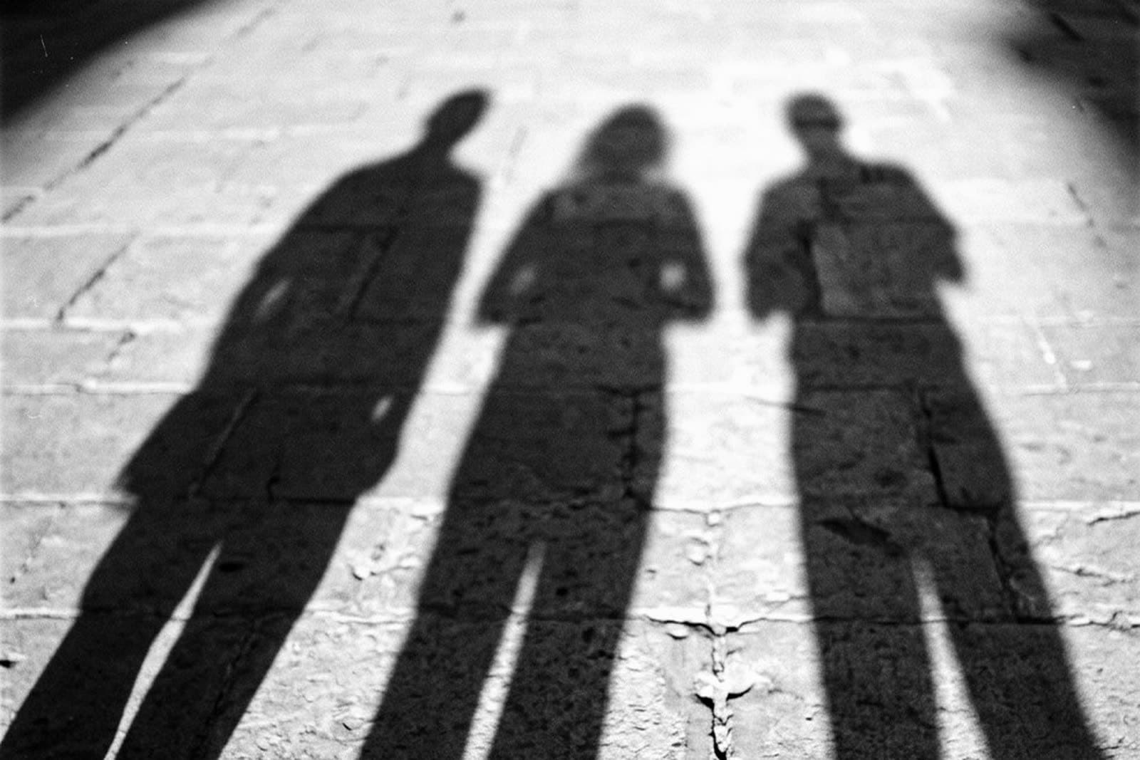 The long shadows of three people standing side by side on worn limestone paving in low sun