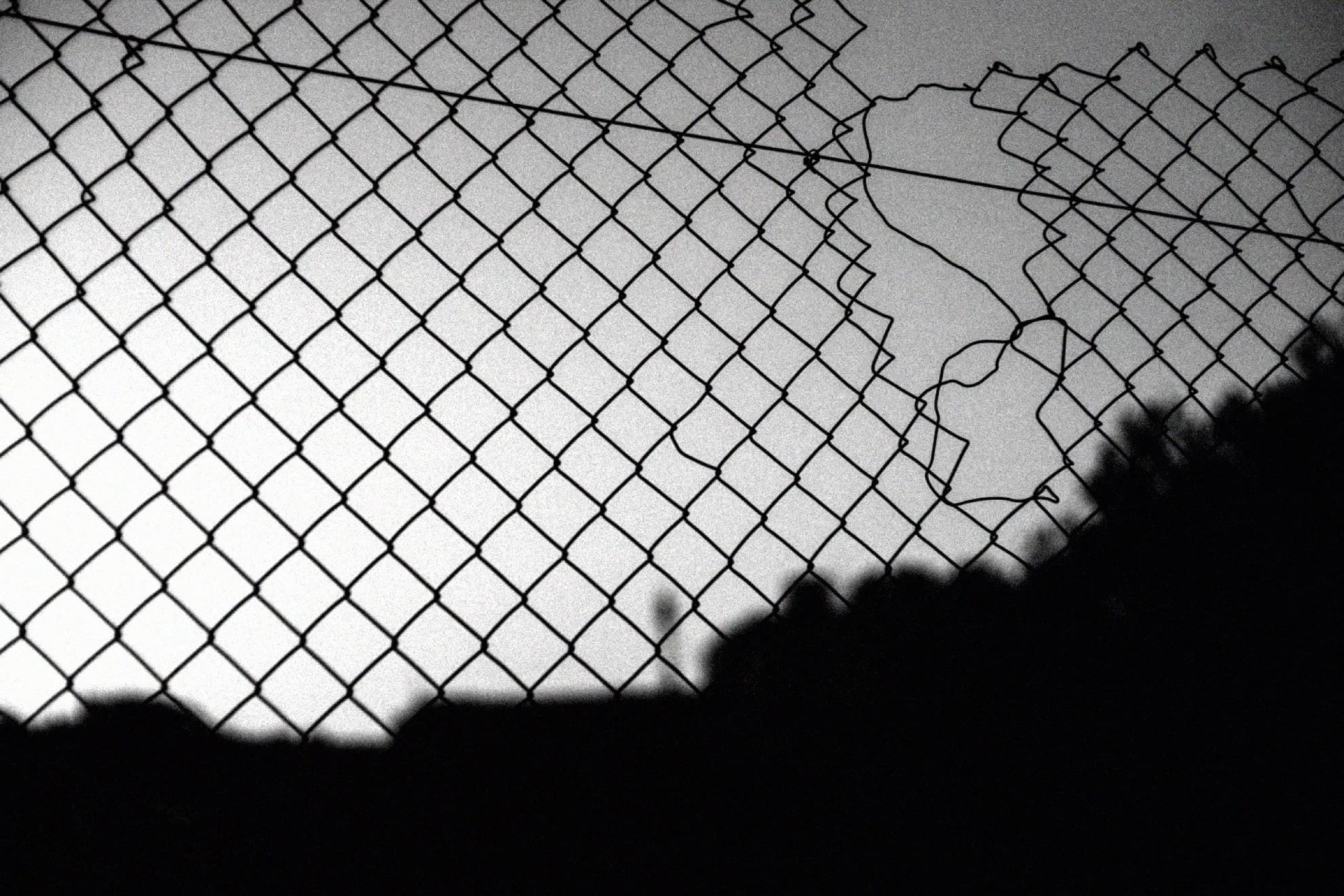 A torn chain-link fence against a bright sky
