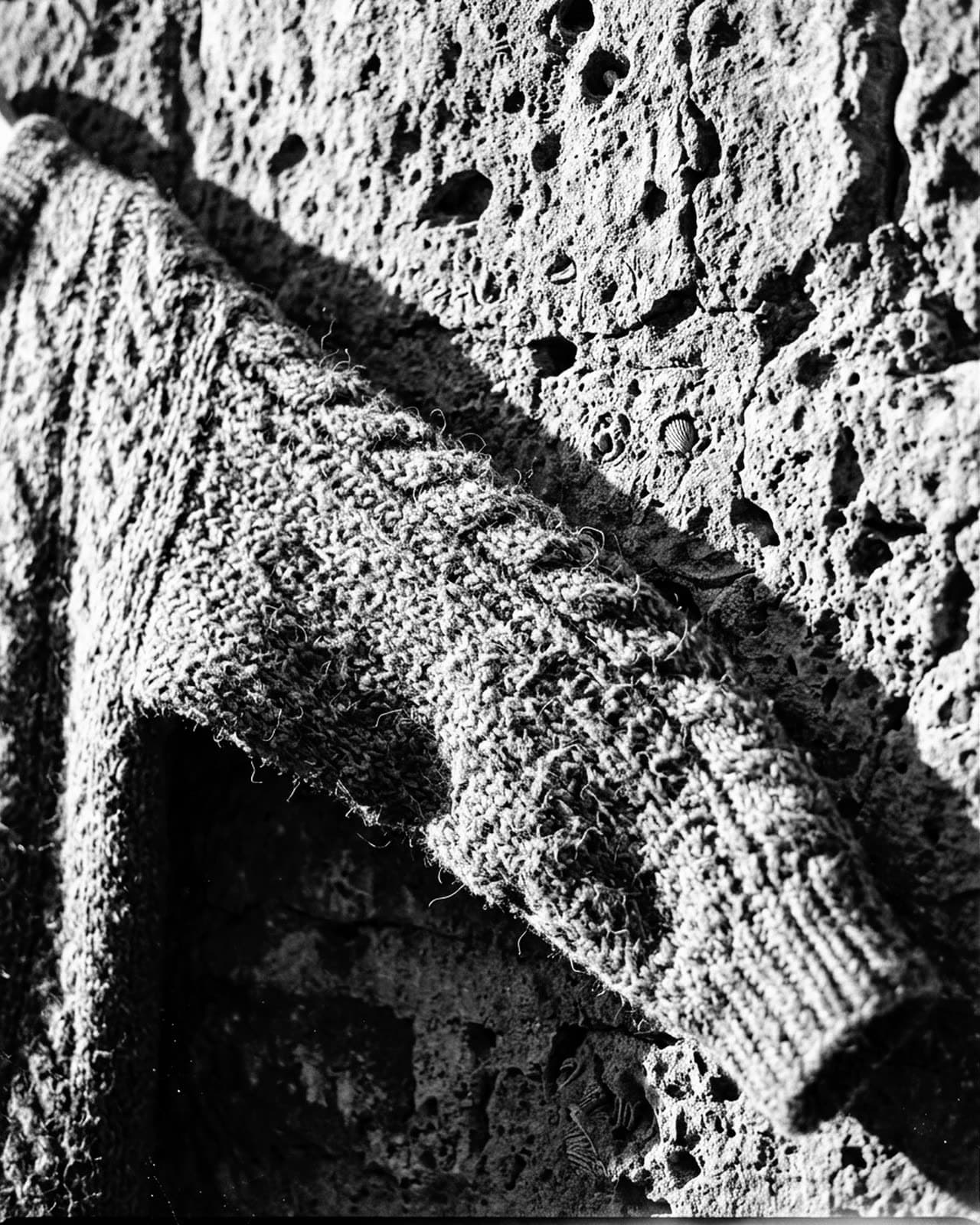 A rough wool sleeve against pitted limestone in raking sun